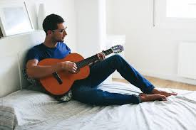 Young man playing guitar sitting on bed at home. by BONNINSTUDIO - Guitarist,  Home - Stocksy United